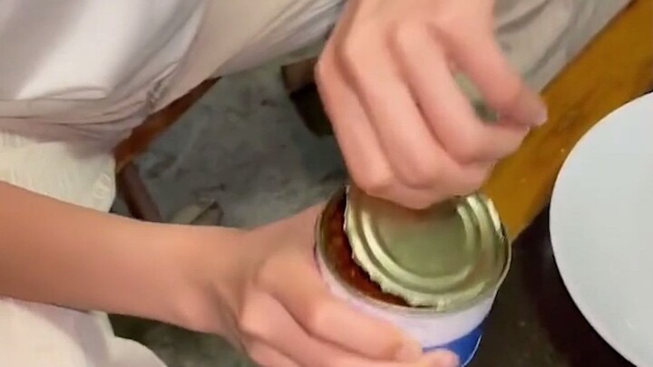 The girl struggled to open the can with a can opener and turned over in confusion. Her brother laugh